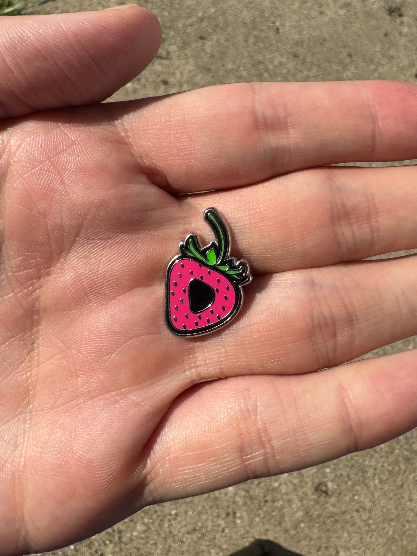 Hand holding a small pink strawberry-shaped object on a concrete surface